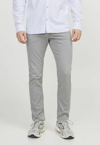 Šedé bavlněné kalhoty s úzkým střihem. Mají hladkou strukturu a kontrastní stehy, doplněné o světlé šedé atletické boty.