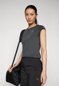 Camiseta ajustada de color gris oscuro con mangas cortas y escote redondo, que presenta un pequeño logo plateado de Puma. Pantalones negros con cordón y una bolsa negra.