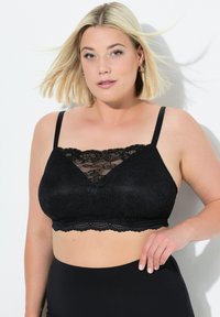Černý krajkový bralet s V-krkem, vlnitými okraji, nastavitelnými ramínky a průhlednou krajkovou tabulí ve přední části. Hladká látková základna.