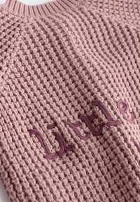 Maglione lavorato a maglia in morbido rosa con una finitura testurizzata. Presenta la scritta ricamata "little" in rosa scuro. Collo rotondo e polsini a coste.
