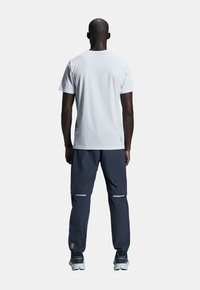 White short-sleeve shirt with a textured design, paired with dark gray pants featuring reflective accents and adjustable cuffs, worn with sneakers.
