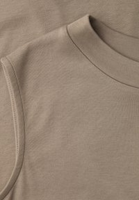 Gros plan sur le tissu beige d'un sweat sans manches montrant les détails de l'encolure ronde et de la couture de l'épaule.