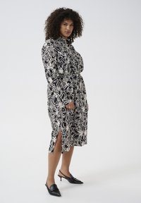 Svartvit blommönstrad klänning med en knapplistdesign, långa ärmar, sidofickor och ett tygbälte. Bärs med svarta slingback-klackar.