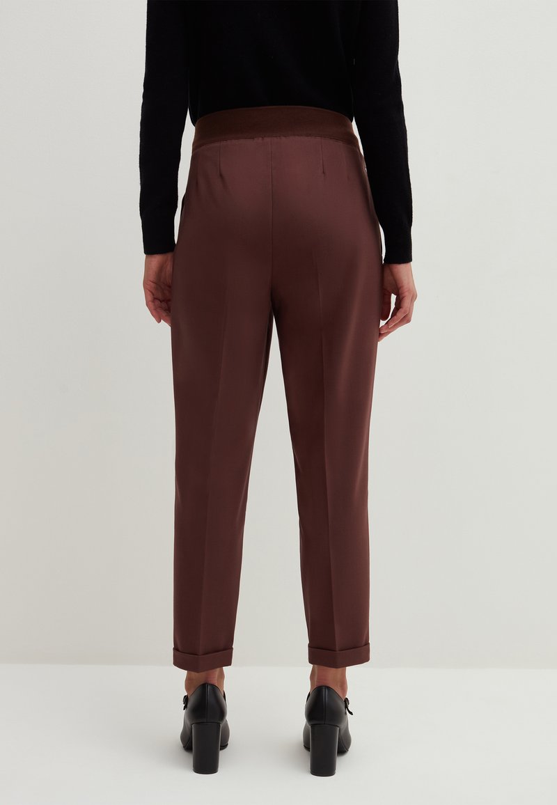Braune Satin-Hosen mit einem gerippten Bund, schmal zulaufenden Beinen und umgeschlagenen Säumen. Tragen kombiniert mit schwarzen High Heels.