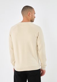 Beige katoenen sweatshirt met raglanmouwen en geribde manchetten. Heeft een ronde halslijn en een rechte zoom zonder zichtbare logo's of patronen.