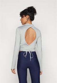 Ljust grå långärmad topp med omslag, öppen rygg och knytning. Matchad med mörkblå högmidjade leggings. Slät textur.