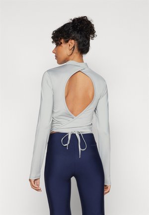 Lys grå langermet topp med innpakningsdesign, åpen rygg og knyting. Parret med mørkeblå høytlivs leggings. Glatt tekstur.