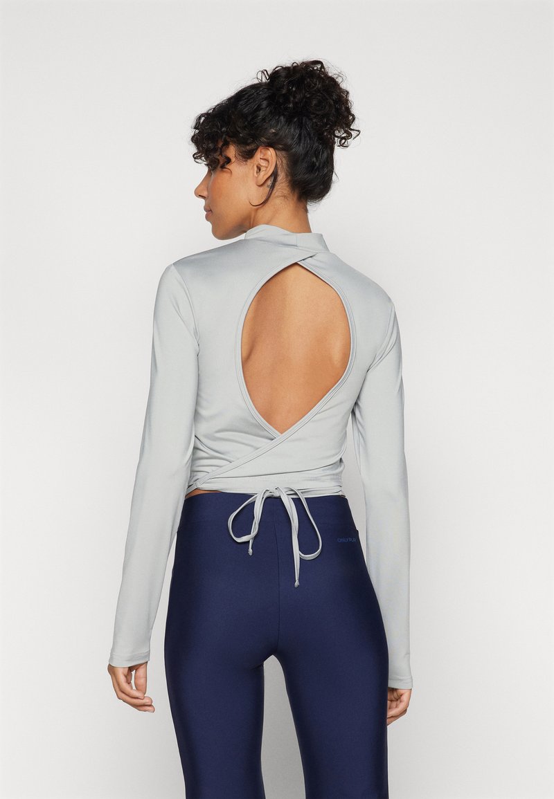 Ljust grå långärmad topp med omslag, öppen rygg och knytning. Matchad med mörkblå högmidjade leggings. Slät textur.