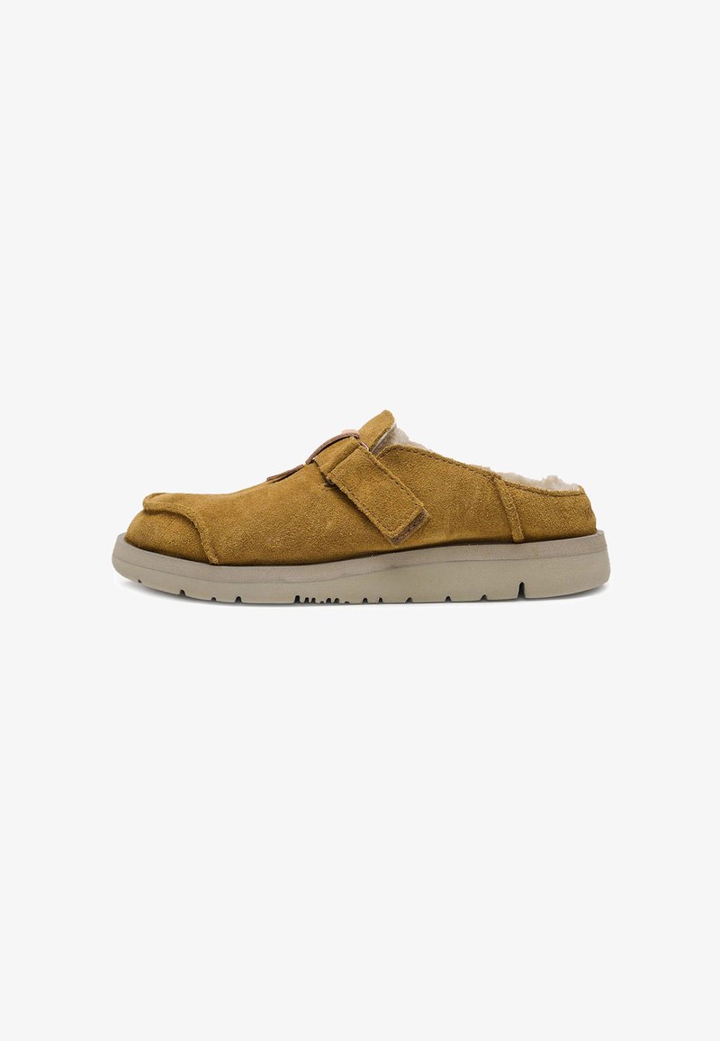 Zapatos de ante marrón tipo slip-on con un interior suave, que cuentan con un cierre de tiras y una resistente suela de goma beige.