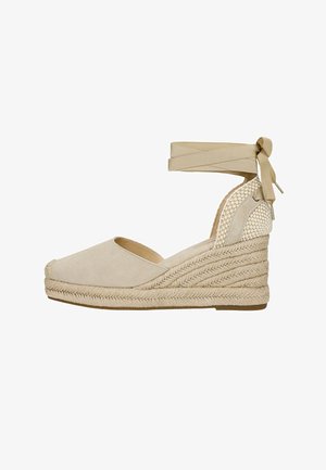 Espadrillas beige con zeppa, punta chiusa, tacco intrecciato, suola in juta intrecciata e cinturino da annodare alla caviglia.