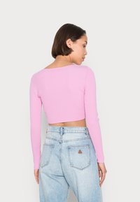 Top cropped canelado rosa com mangas longas, apresentando um decote largo, emparelhado com jeans de cintura alta azul claro com um remendo em triângulo na parte de trás.
