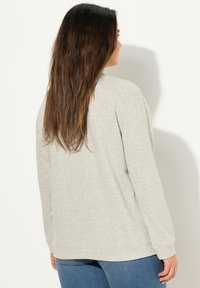 Felpa grigia chiara con maniche lunghe, scollo a brodo e polsi a costina. Tessuto morbido con vestibilità comoda. Orlo morbido e nessun motivo visibile.
