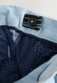 Jasnoniebieska tkaninowa talia z czarnym guzikiem i paskowanym akcentem. Wnętrze wyściełane granatową podszewką z zygzakowatym wzorem.