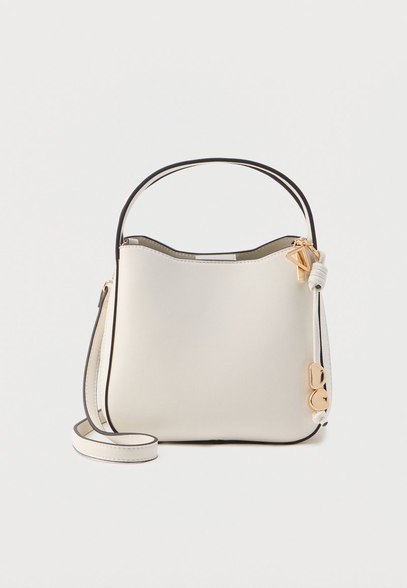 Sac à main en cuir couleur crème avec garniture noire, poignée courte, bandoulière amovible et breloques décoratives dorées sur une sangle nouée.