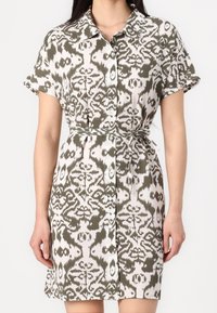 Robe chemise en motif ikat vert et blanc, manches courtes, fermeture à boutons sur le devant, taille cintrée avec une ceinture en tissu assorti, longueur genoux.