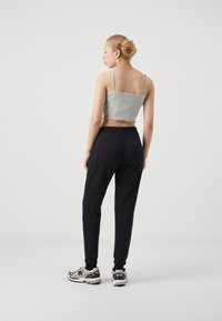 Gray cropped tank top with frayed hem, paired with black tapered joggers. Model wears patterned athletic shoes, facing away from the camera.
