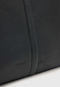 Juoda odinė rankinė su tekstūruotu paviršiumi, kurioje subtiliai iškaltos "ALLSAINTS" ir "LONDON" logotipai palei siūlę.