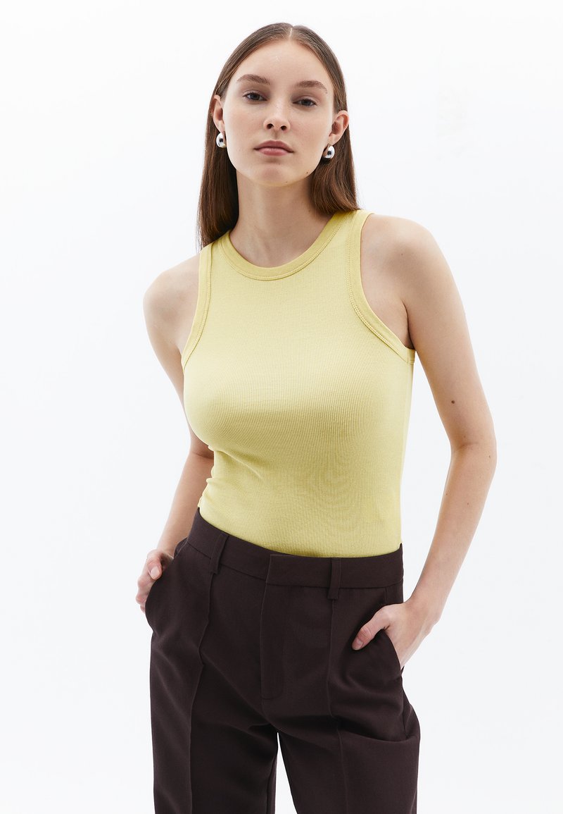 Ljusgul ribbad linne med rund halsringning och ärmlös design, kombinerad med mörkbruna skräddarsydda byxor.