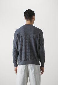 Szary sweter z długim rękawem z teksturowanym wzorem nazwy marki, z prążkowanymi mankietami i pasem. Luźny krój, lekka tkanina.