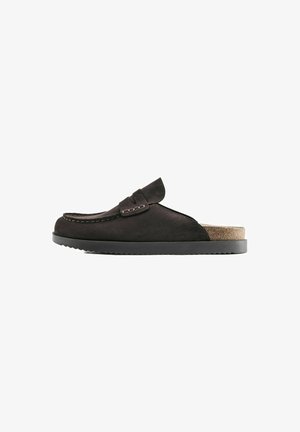 Mocassin marron foncé en daim à enfiler avec une couture moc toe, une semelle à faible adhérence et un talon de semelle intérieure en liège partiellement visible.