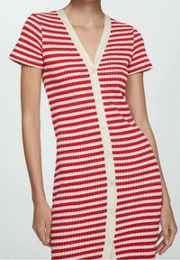 Robe rayée rouge et blanche avec des manches courtes, en tissu tricoté texturé, décolleté en V, et une rangée de boutons sur le devant. Finition crème.