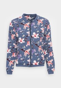Giacca bomber floreale blu con fiori rosa e viola e farfalle bianche, chiusura con zip, polsini e orlo a costine. Tessuto morbido.