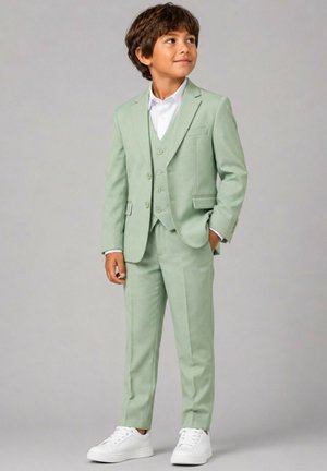 Jeune garçon portant un costume trois pièces vert clair avec une chemise blanche et des baskets blanches, debout avec une main dans la poche.