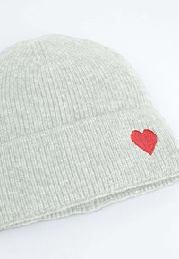 Berretto a coste grigio con una toppa a forma di cuore rosso sul lato. Tessuto morbido, design aderente, adatto per il clima freddo.