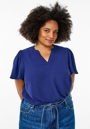 Navy blue short-sleeve blouse with a v-neck and textured leopard print pattern; worn with high-waisted denim jeans featuring a tie waist.