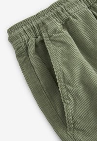Olijfgroene corduroy broek met een elastische tailleband, voorzien van zijzakken en een ribbelachtige textuur voor extra detail.