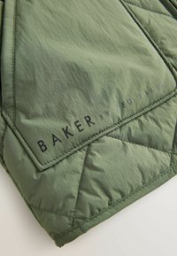 Zaļa izšūta jaka ar gludu tekstūru, kurai ir melns "BAKER by TED BAKER" logotips. Ietver leņķveida šuvju rakstu.