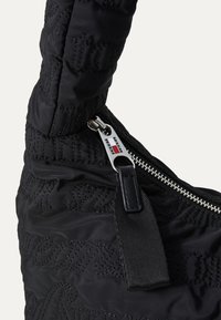 Sac à main noir matelassé avec un design de texte en relief, une fermeture éclair en argent avec un tirant de marque, et une finition en tissu texturé.