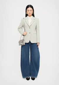 Ljust grå kavaj med en strukturerad design, guldknappar, kombinerad med vida blå denimjeans. Accessoarer inkluderar en liten silverhandväska.