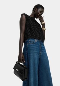 Top corto negro texturizado con patrón en zigzag, combinado con unos pantalones vaqueros de pierna ancha azul de cintura alta. Sosteniendo un pequeño bolso negro con acentos plateados.