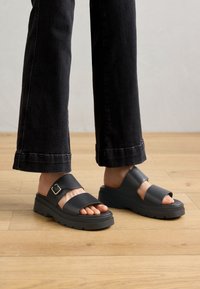Sorte sandaler med to brede stropper, en spenne og en kraftig såle. Designet har en glatt tekstur med et solid grep.