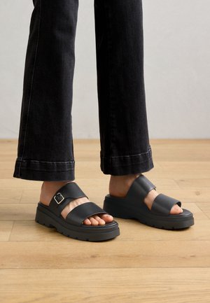 Sandalias negras con dos correas anchas, un detalle de hebilla y una suela gruesa. El diseño presenta una textura suave con un agarre resistente.