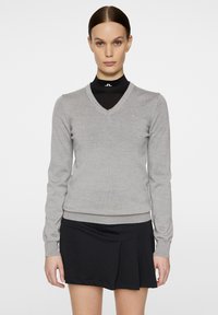 Harmaa V-kaulusneule, joka on valmistettu pehmeästä neulemateriaalista. Siinä on pitkät hihat ja slim fit -muotoilu, yhdistettynä mustiin hamehousuihin.