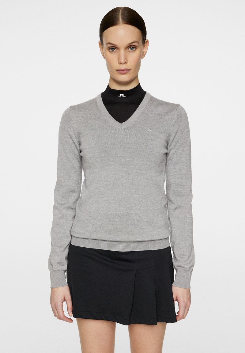 Harmaa V-kaulusneule, joka on valmistettu pehmeästä neulemateriaalista. Siinä on pitkät hihat ja slim fit -muotoilu, yhdistettynä mustiin hamehousuihin.