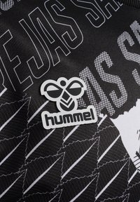 Zwarte stof met abstracte witte patronen. Een prominent grijze en zwarte "hummel" logo-tag met een gestileerd bijontwerp is zichtbaar.