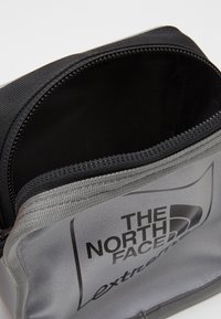 Pochette nera e grigia realizzata in tessuto resistente, con apertura a zip e logo impresso sul davanti, caratterizzata da una finitura testurizzata.