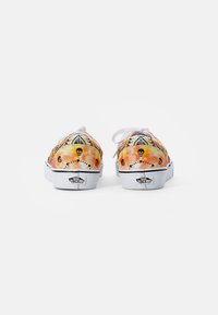 Sneakers med et fargerikt mønster som viser hodeskaller, i oransje og gule nyanser, hvite snører og en hvit gummisåle med svarte detaljer.