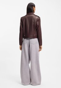 Burgundy leather cropped jacket with shoulder epaulets, paired with wide-leg pale gray trousers. Smooth texture and tailored fit are visible.