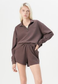 Brun, teksturert zip-up hettegenser med krage og matchende shorts. Stoffet ser mykt og avslappet ut med strikket midje.