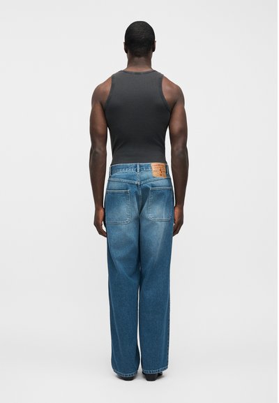 Modré džínsové rifle s voľným strihom, širokými nohavicami a dvoma zadnými vreckami. Pás má hnedú koženú značku s detailmi značky.