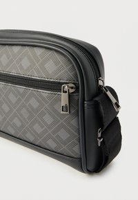 Μαύρη και γκρι τσάντα με υφασμένο γεωμετρικό μοτίβο, διαθέτει επάνω φερμουάρ, ρυθμιζόμενο λουρί και κομψές άκρες. Χρησιμοποιούνται ανθεκτικά υλικά.