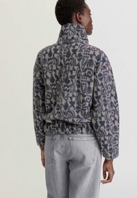 Fleece pullover met hoge kraag, met een blauw en grijs abstract patroon. Relaxte pasvorm, geribde zoom en zachte textuur. Draag met lichtgrijze jeans.