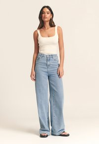 Gaiši krāsots ribots krekls ar kvadrātveida izgriezumu, savienots ar augsta vidukļa, plaša kāju apjoma gaiši zilām džinsa biksēm. Melnas plakanas sandales. Gludas tekstūras.