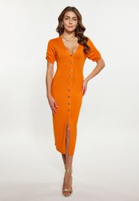 Rochie midi tricotată de culoare portocalie, cu mâneci scurte tip puff, decolteu adânc în V, detalii cu nasturi pe față și fante laterale. Accentuată cu nasturi aurii strălucitori.