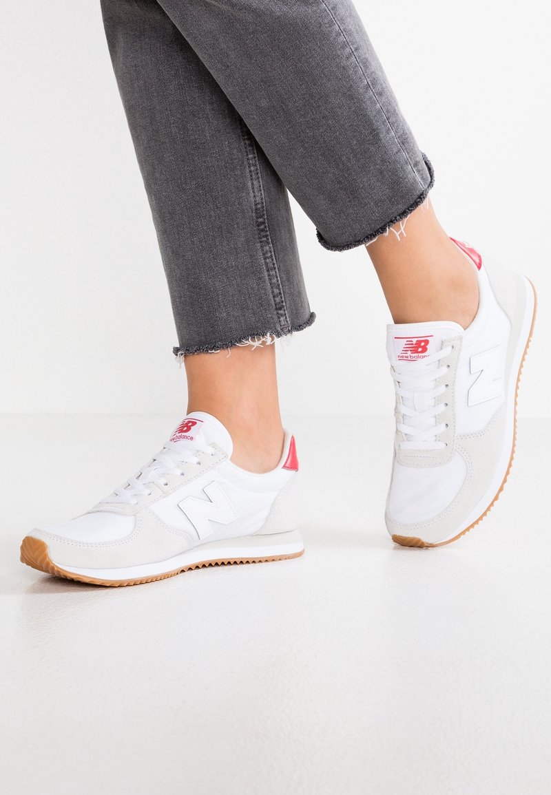 Baskets blanches avec des accents roses et des détails en daim gris, dotées d'une semelle extérieure en gomme texturée, d'un design à lacets et d'un logo "N" bien visible.