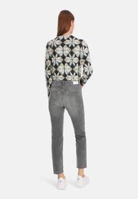 Geprinte trui met een geometrisch ontwerp in zwart, wit, groen en blauw. Grijze denim broek en witte sneakers maken de outfit compleet.
